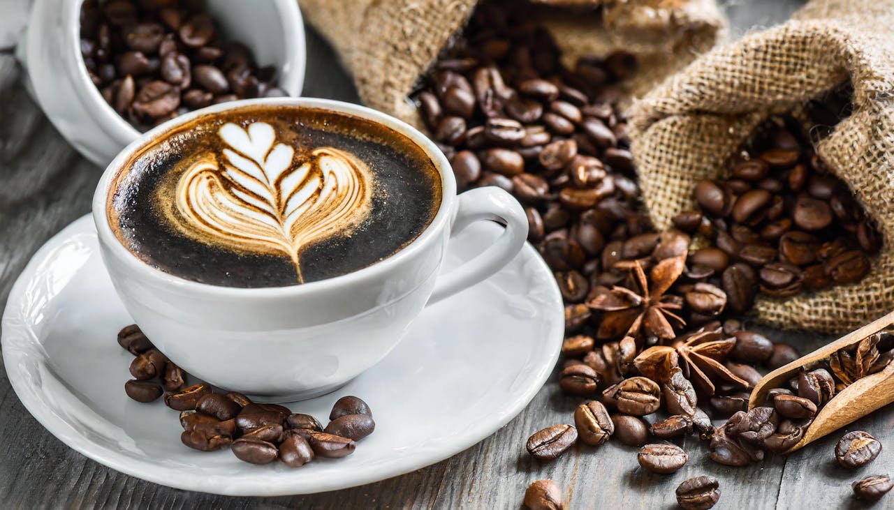 A beautifully decorated cappuccino with latte art surrounded by coffee beans on rustic background.